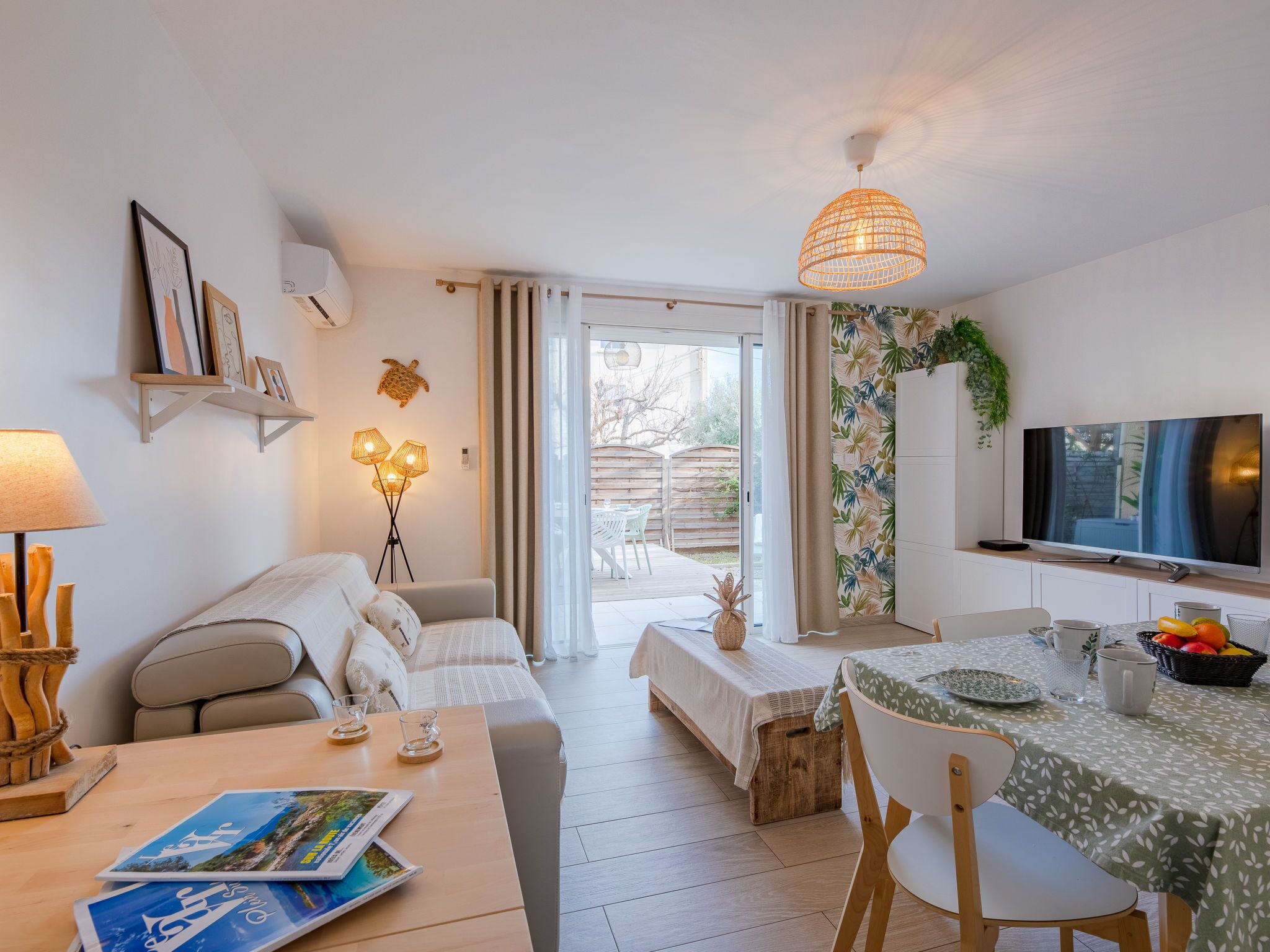Una sala de estar moderna con un sofá, una mesa de comedor y un televisor. Hay un balcón con vistas al exterior.