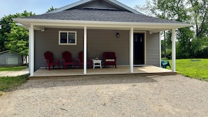 A covered porch with four red Adirondack chairs, a small table, and a door leading to the house.