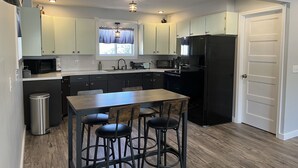 A compact kitchen with a central island, bar stools, a refrigerator, and a microwave.