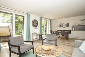 A modern living room with grey sofas, a round coffee table, and a dining area with chairs.