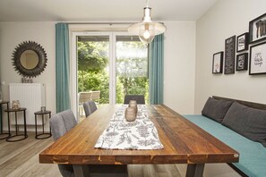 Un comedor con una mesa de madera, sillas, un jarrón y una lámpara colgante.