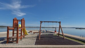 A playground with a slide and swings by a calm body of water. - Sea side by Interhome (Pašman/Kraj)