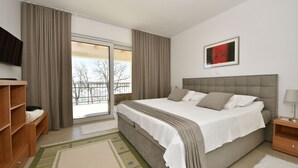 A bedroom with a large bed, a television on the left, a wooden nightstand, and a view of a balcony. - Sea side by Interhome (Pašman/Kraj)