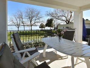 A balcony with a white table and chairs, a vase with flowers, and a view of a lake and trees.