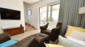 A modern living room with leather furniture, a flat-screen TV, a staircase leading to a balcony, and a view of greenery outside. - Sea side by Interhome (Pašman/Kraj)