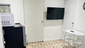Een compacte woonruimte met een kitchenette, een flatscreen televisie aan de muur, een eettafel met stoelen en een bank.