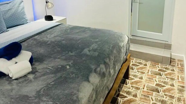 Een slaapkamer met een bed, nachtkastje, lamp, schilderij en een deur.