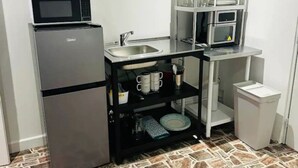 Een kleine keuken met een koelkast, magnetron, spoelbak en een wandplankje met servies en bekers.