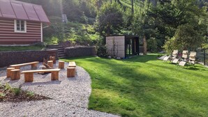 A cabin with a red exterior, a wooden deck with benches, a small wooden structure, and a grassy area with lounge chairs. - Charming Mountain Lodge & Wellness by Interhome (Horní Maršov/Pec pod Sněžkou)