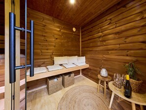 A wooden cabin interior with a wooden bench, towels, baskets, a woven rug, a small table with a bottle of wine, and glasses. - Charming Mountain Lodge & Wellness by Interhome (Horní Maršov/Pec pod Sněžkou)