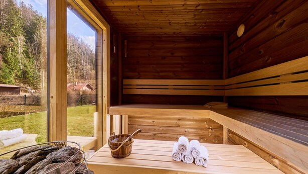 A wooden sauna with benches, a table with towels and a bucket, and a view of a forested area. - Charming Mountain Lodge & Wellness by Interhome (Horní Maršov/Pec pod Sněžkou)