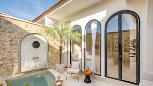 A pool area with a stone wall, a chair, a table with a tray, and large arched windows. - Romantic Villa - Ultimate Love Sanctuary (Canggu)