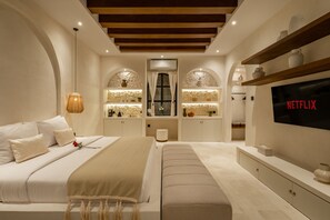 Un dormitorio moderno con una cama grande, un televisor montado en la pared y estanterías empotradas con objetos decorativos.