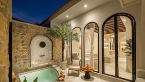 A luxurious outdoor pool area with a stone wall, a palm tree, and a cozy seating area with a table and chairs. - Romantic Villa - Ultimate Love Sanctuary (Canggu)