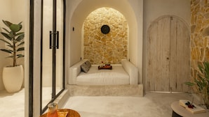 A modern interior with a stone wall, a white cushioned bench, a wooden door, and a potted plant. - Romantic Villa - Ultimate Love Sanctuary (Canggu)