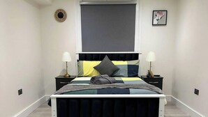 A bedroom with a bed, two bedside tables, a window, a clock, and a framed picture on the wall.