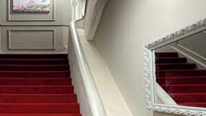 A staircase with red carpeted steps and a white wall.