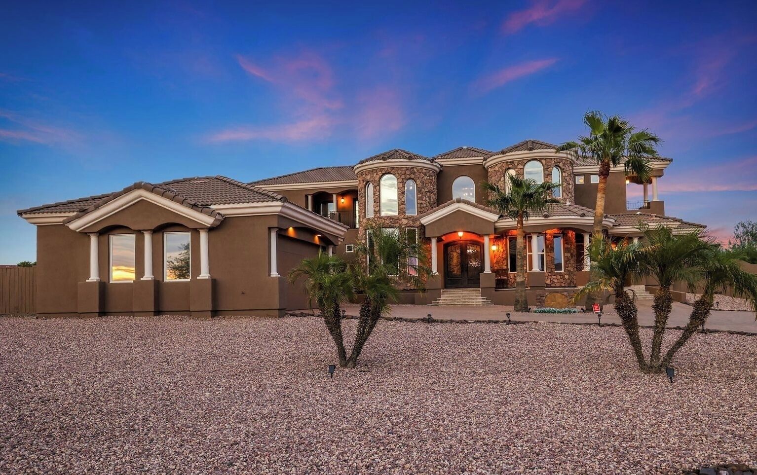 A large, multi-story house with a stone facade, multiple windows, and a well-maintained gravel driveway.