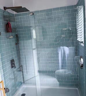 A bathroom with a glass shower enclosure, a tiled wall, and a red fire extinguisher on a shelf.