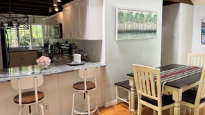 Una cocina con armarios blancos, encimera de mármol y comedor con mesa y sillas.
