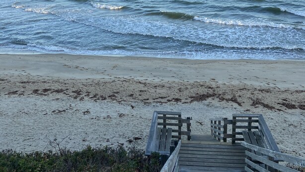 Una pasarela de madera que conduce a una playa, con olas al fondo.