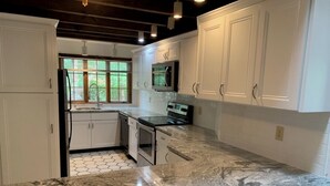Cocina con armarios blancos, encimera de granito y ventana con vistas al verdor.