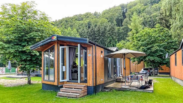 Une cabane en bois avec un patio, une table et des chaises, et un chien allongé sur l’herbe.