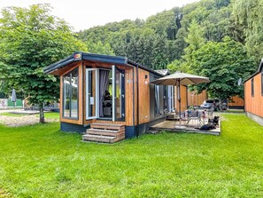 A wooden cabin with a patio area, a table with chairs, and a dog lying on the grass.