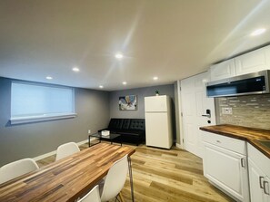 A compact kitchen with white cabinets, a built-in microwave, and a wooden dining table with chairs.