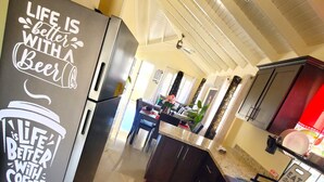 Una cucina moderna con elettrodomestici in acciaio inossidabile, un piano di lavoro in granito e una parete protettiva. Ci sono due tappetini rossi sul pavimento e un cartello sul frigorifero con su scritto: “La vita è meglio con la birra.”