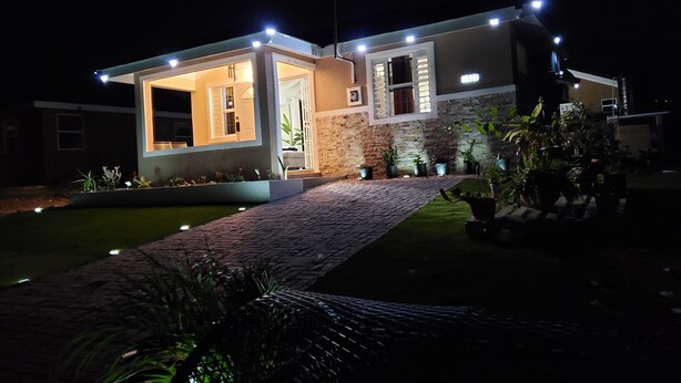 Una casa moderna con un ingresso luminoso, un vialetto lastricato e piante in vaso intorno alla proprietà.