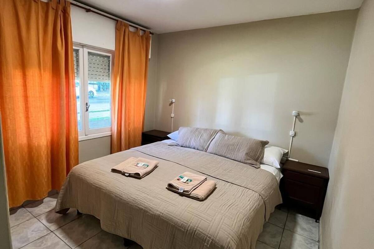 A bedroom with a bed, a nightstand, a window with curtains, and a ceiling light.