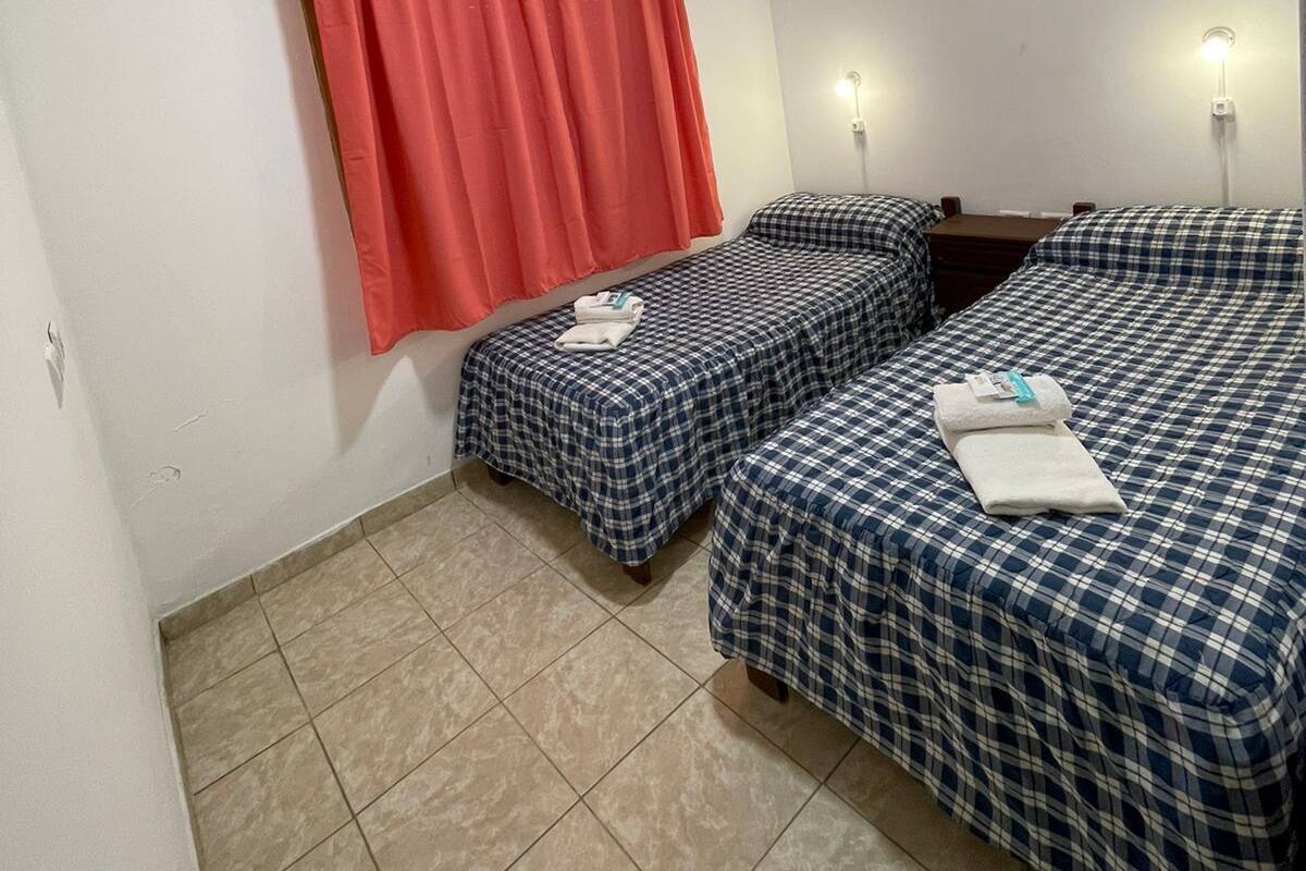 A small, clean room with two beds, a red curtain, and a ceiling light.