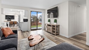 A modern living room with a grey sofa, a wooden coffee table, and a TV mounted on the wall. There is a sliding glass door leading to a patio area. - Cozy 3-bedroom house in peaceful Renton with WiFi, AC (Renton)