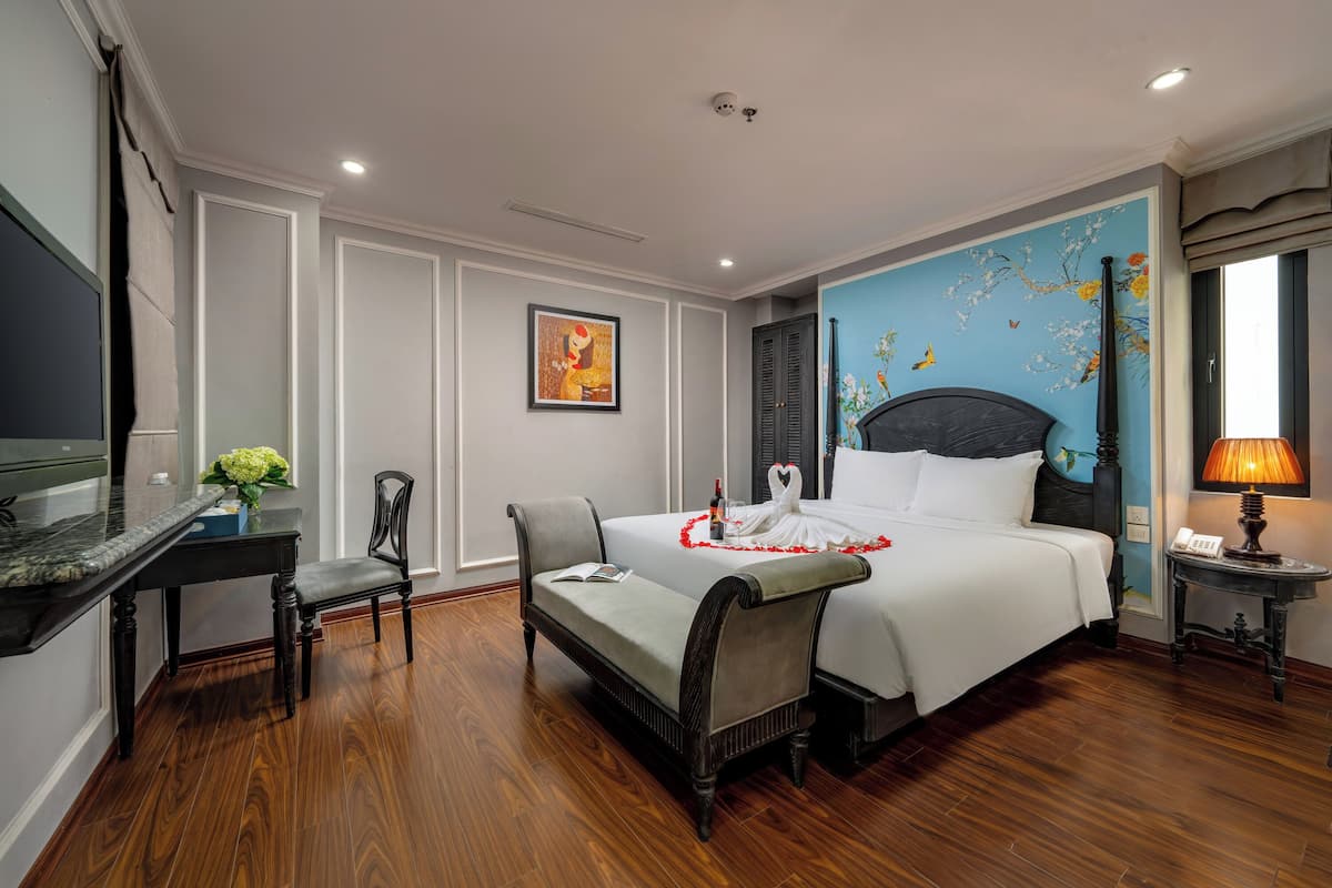 Une chambre d’hôtel avec un grand lit, un bureau, une chaise, une petite table avec une lampe et un élément décoratif mural.