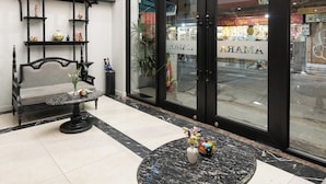 Um hall com piso de mármore, uma mesa redonda com um vaso, um banco e um candelabro.