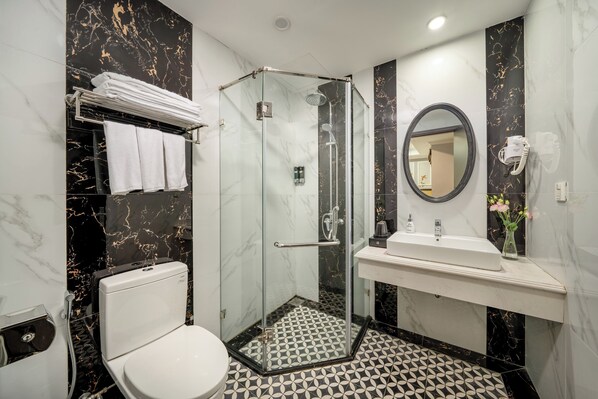 Un baño moderno con ducha envuelta en vidrio, inodoro blanco, lavamanos con espejo y toallero.