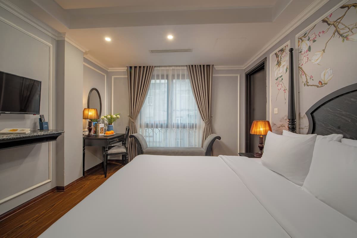 Une chambre d’hôtel avec un grand lit, un bureau avec une chaise, une télévision et une fenêtre avec des rideaux.
