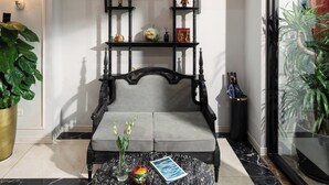 Um banco de madeira preta com uma mesa de mármore na frente, uma planta em vaso à esquerda e uma grande janela à direita.