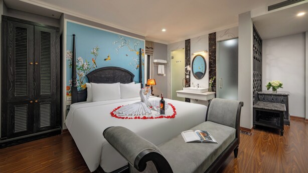 Quarto de hotel com uma cama grande, um sofá, banheiro com espelho e uma pequena lareira.
