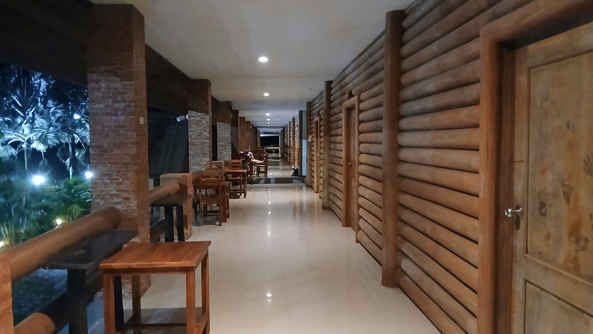 Un pasillo con paneles de madera, pared de ladrillo y un rincón de descanso con mesas y sillas.