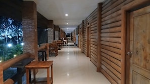 A corridor with wooden paneling, a brick wall, and a seating area with tables and chairs. - Vang Vieng Romantic Mountain View Resort (Vang Vieng)