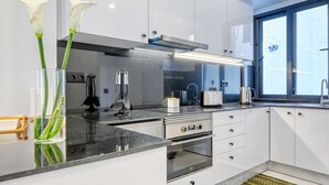 A modern kitchen with white cabinets, a stainless steel range, and a large window. - Beco Santa Emilia 2H, a Home in Madeira (Funchal)