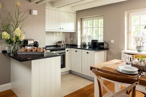 A modern kitchen with white cabinetry, a black countertop, and a dining area with a wooden table and chairs. - Südfall - Ein Kuschelnest für Zwei Erwartet Sie in Tinnum (Tinnum)