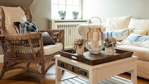 Una sala de estar acogedora con una silla de mimbre, un sofá blanco y una mesa de centro de madera con objetos decorativos.