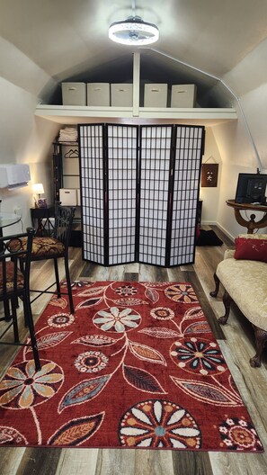 A room with a traditional Japanese shoji screen, a wooden dining table, a red patterned rug, and a ceiling fan.