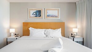 Quarto de hotel com cama, duas mesas de cabeceira, encosto de cama de madeira e duas imagens emolduradas na parede.