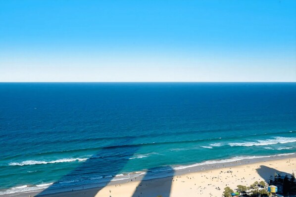 A beach with clear blue water, a sandy shore, and a few buildings in the distance.