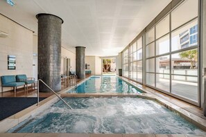 An indoor swimming pool with a view of the outside, a seating area with chairs, and a large pillar.
