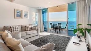 Uma sala de estar moderna com um sofá, mesa de centro e varanda com vista para o mar.